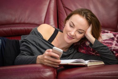 Smiling pretty woman reading book and using mobile phone