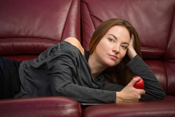 Beautiful relaxed woman lying on sofa and eating apple — Stock Photo, Image