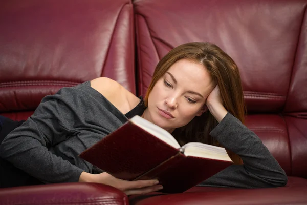 Attractive young woman resting on sofa and reading a book — 图库照片