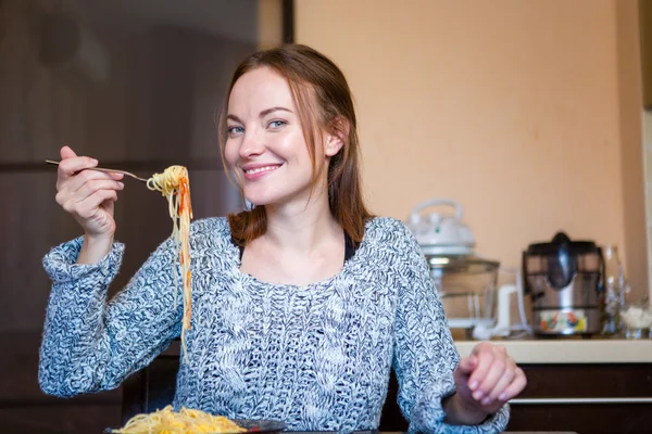 Gyönyörű vidám fiatal nő eszik tésztát, konyha — Stock Fotó