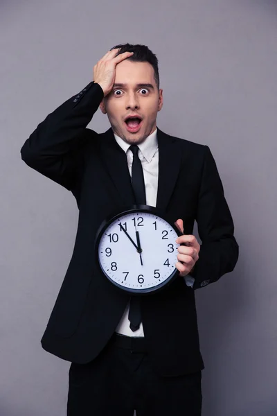 Hombre de negocios sorprendido sosteniendo reloj de pared —  Fotos de Stock