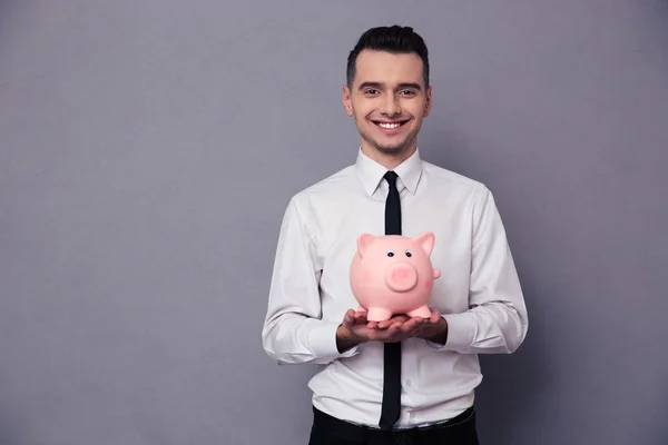 Hombre de negocios sonriente sosteniendo caja de dinero de cerdo — Foto de Stock