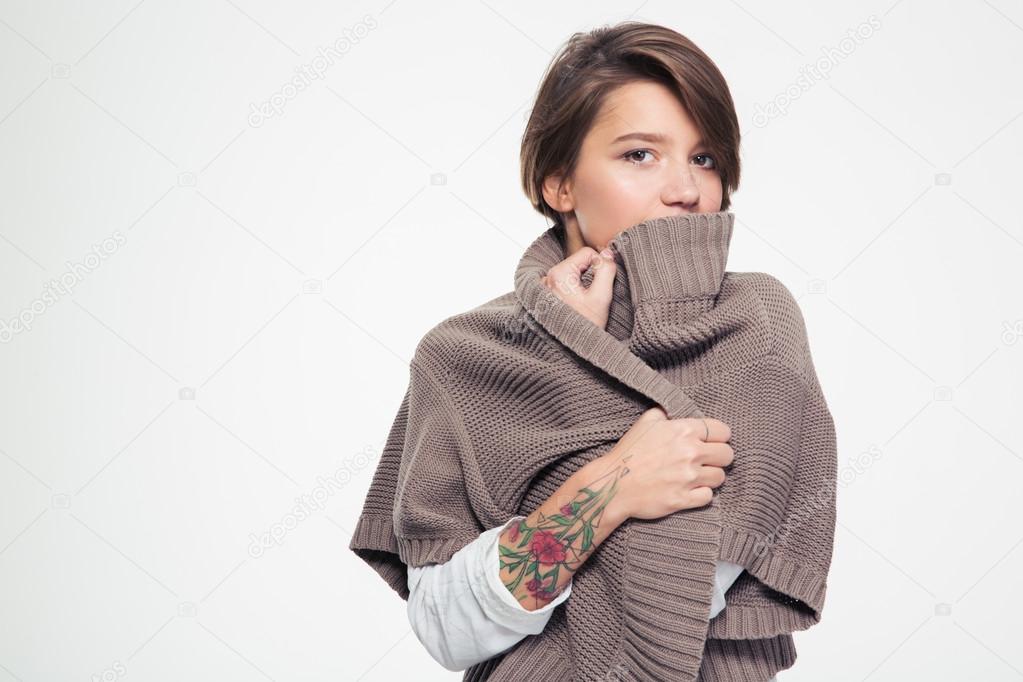 Pensive sad woman with tatoo hiding lipd behind knitted jacket 