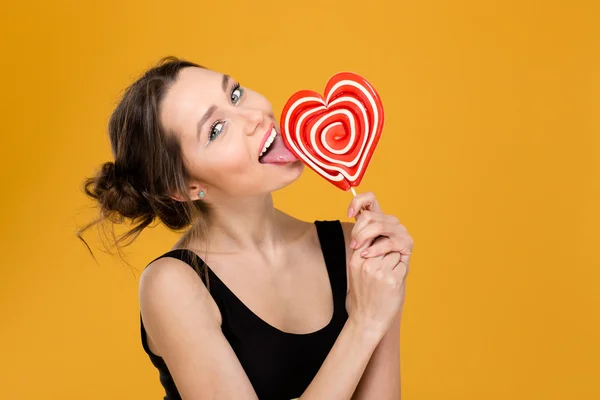 Lovely playful woman licking sweet heart shaped lollipop — Stock Photo, Image