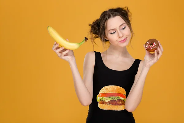 Jovem pensativa confusa escolhendo entre alimentos saudáveis e não saudáveis — Fotografia de Stock