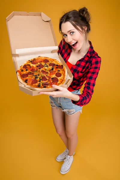 Mooie lachende jonge vrouw permanent en tonen pizza — Stockfoto