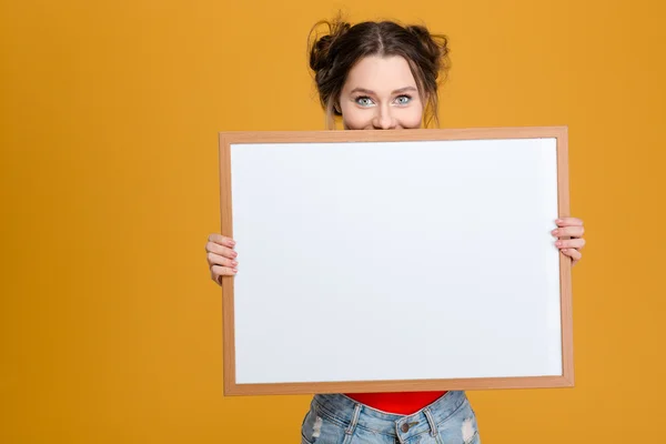 Souriant mignon belle jeune femme cachée derrière le tableau blanc — Photo