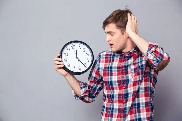Беспокойный мужчина в клетчатой рубашке держит и смотрит на часы — стоковое фото
