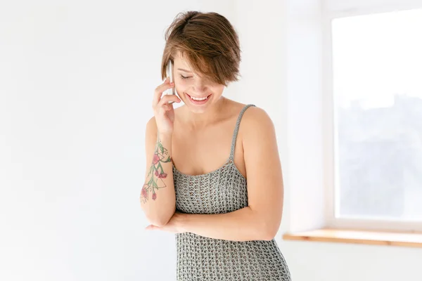 Mulher alegre encantadora falando no telefone celular perto da janela — Fotografia de Stock