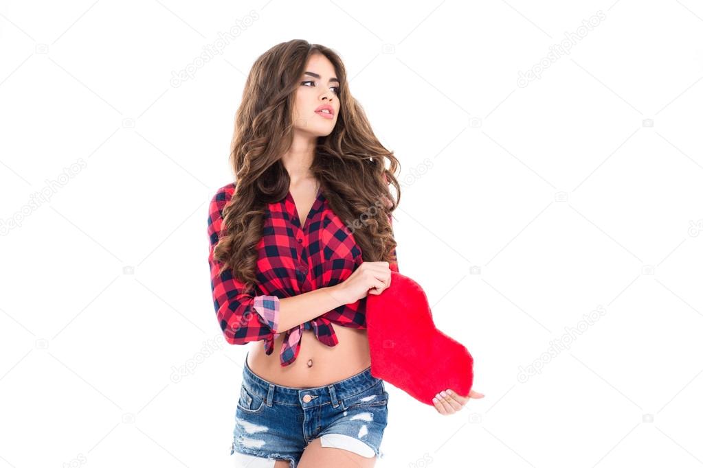 Pensive pretty young woman holding red heart 