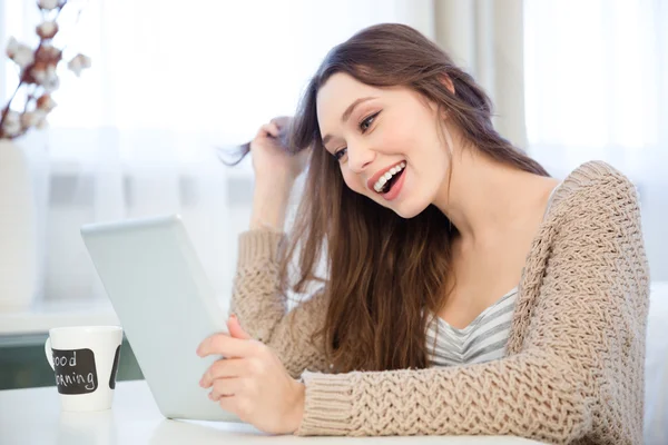 Привлекательная веселая молодая женщина с планшетом и смеясь дома — стоковое фото