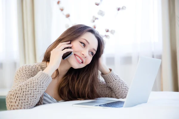 Bella donna sorridente utilizzando il cellulare e il computer portatile a casa — Foto Stock