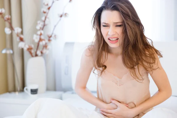 Beautiful young woman sitting and suffering from abdominal pain — Stock Photo, Image