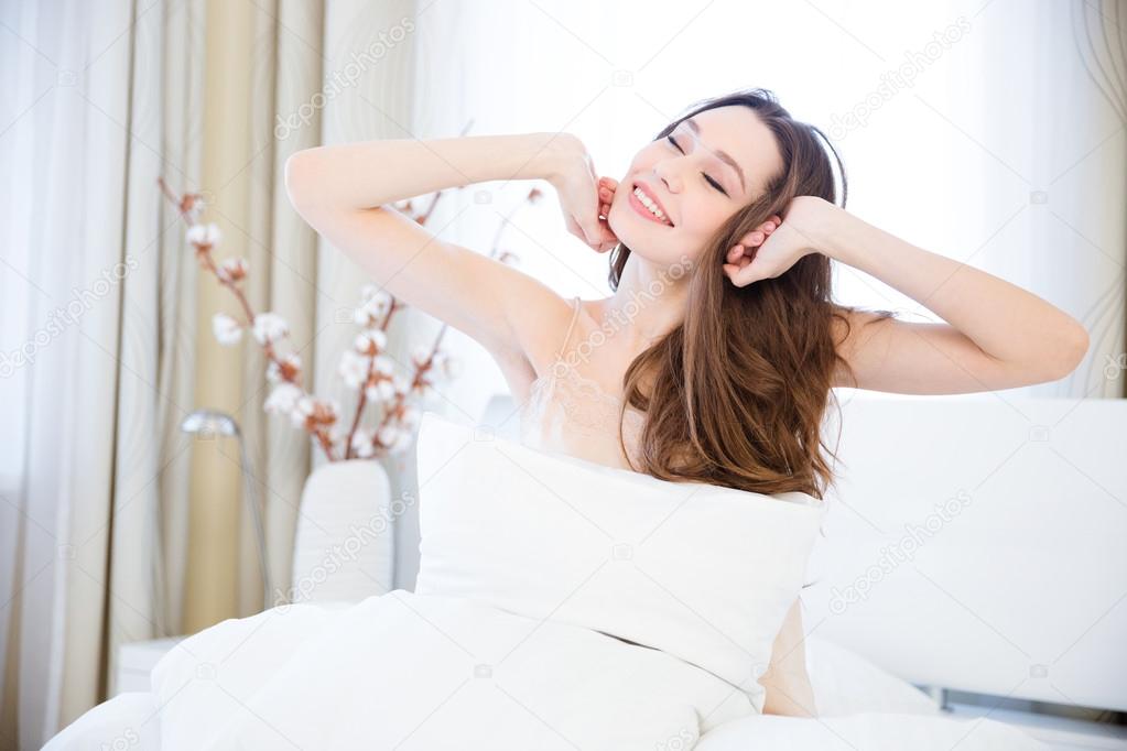 Tender woman waking up and stretching on bed in bedroom