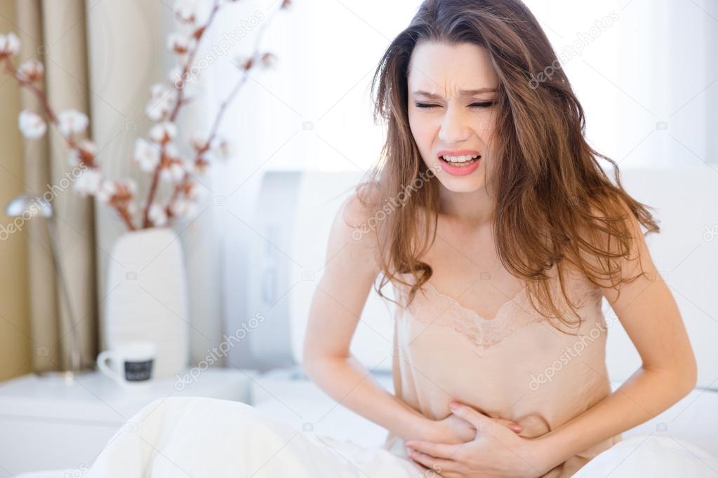 Beautiful young woman sitting and suffering from abdominal pain 