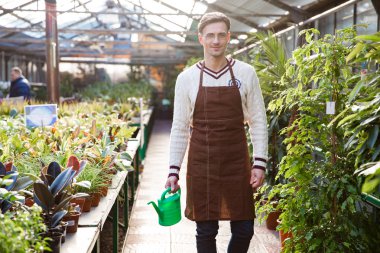 Smiling man gardener standing and holding watering can in orangery