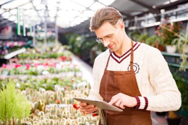 Attractive man gardener standing and using tablet