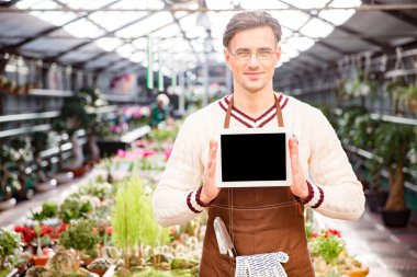 Gardener showing blank screen tablet in greenhouse