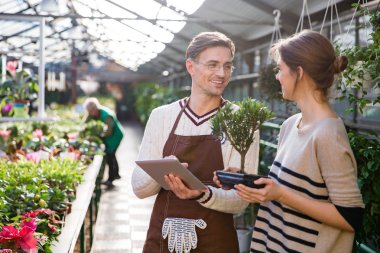 Gardener using tablet and talking with woman holding bonsai tree