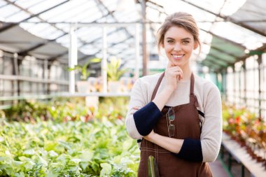 Happy beautiful woman gardener standing in greenhouse