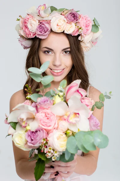 Lovely cheerful female in rose wreath showing bouquet of flowers — Stock Photo, Image