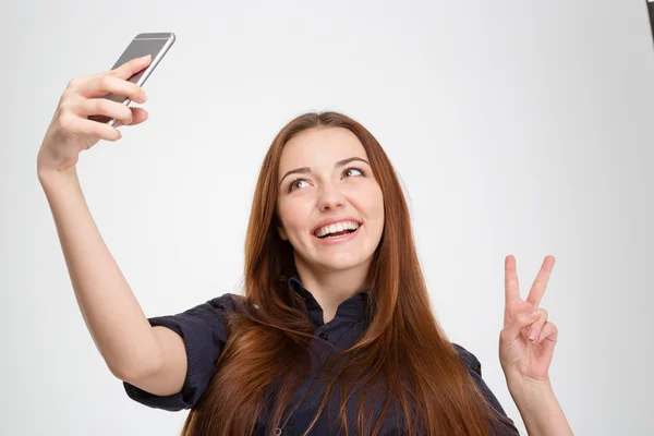 Smiling woman taking selfie with mobile phone showing victory sign — Stock Photo, Image
