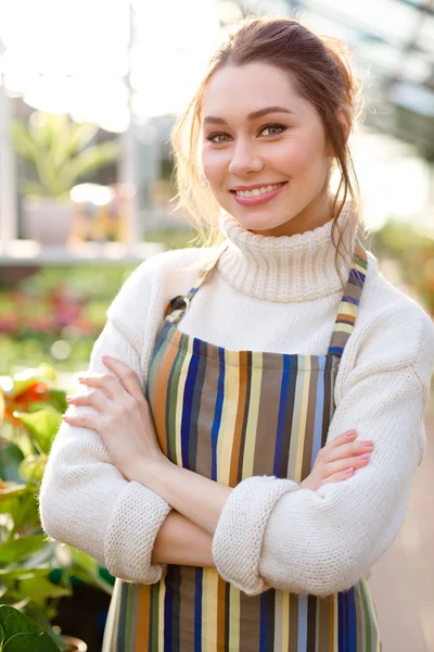 Jardineiro de uma linda mulher sorridente em pé com os braços cruzados em estufa — Fotografia de Stock