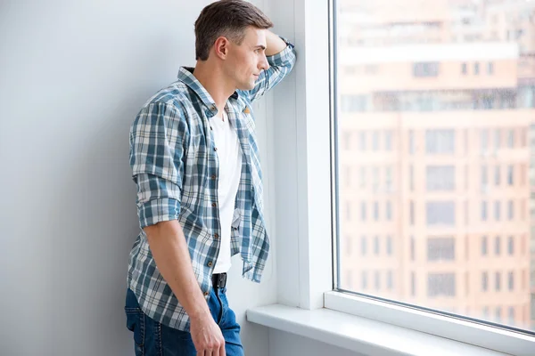 Pensive handsome man standing near the window — Stock Photo, Image