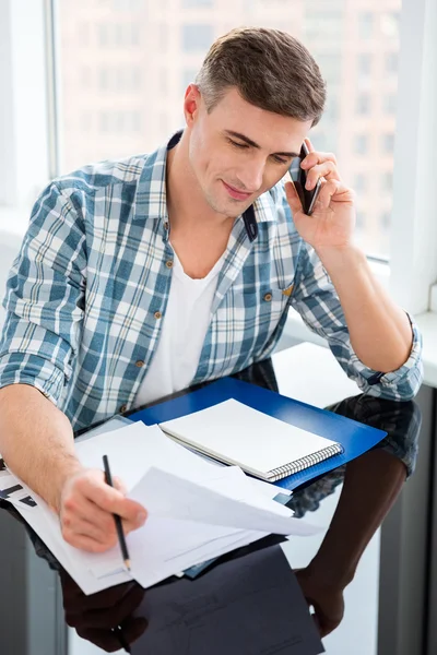 Selbstbewusster Mann sitzt mit Rechnungen und telefoniert — Stockfoto