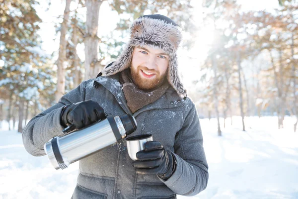 Hombre feliz bebiendo té caliente del termo en el parque de invierno —  Fotos de Stock