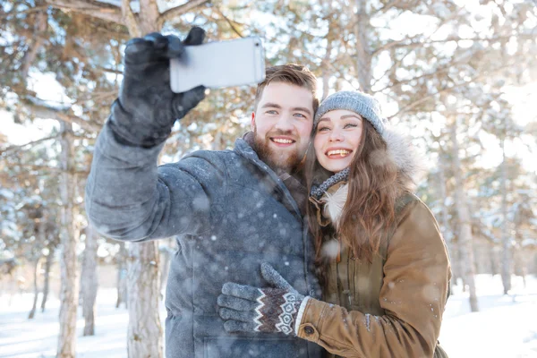 Пара робить фотографії на смартфоні в зимовому парку — стокове фото