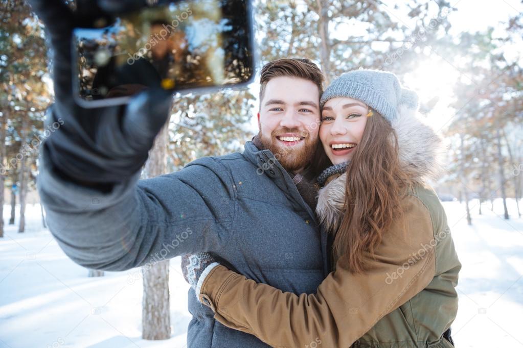 Couple making photo on smartphone in winter park