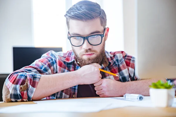 Pensive bearded engineer sitting at the table and creating blueprint — Stock Photo, Image