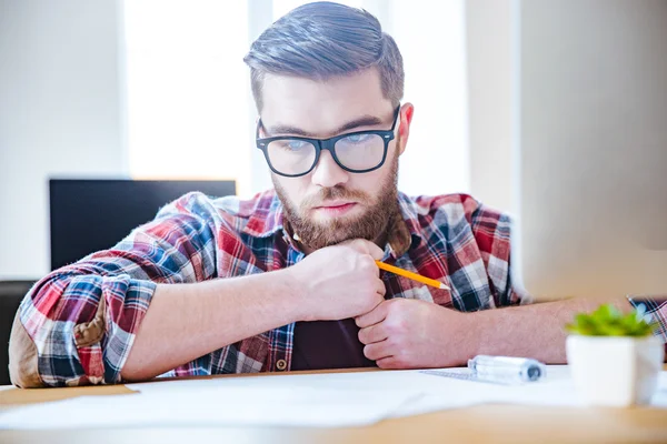 Nadenkend bebaarde ingenieur zitten aan de tafel en het creëren van blauwdruk — Stockfoto