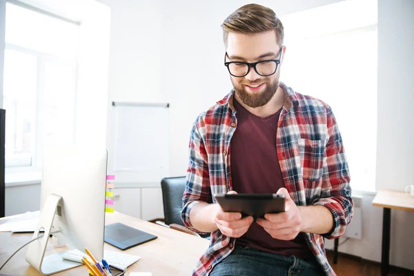 Homem bonito feliz com barba sentado e usando tablet — Fotografia de Stock