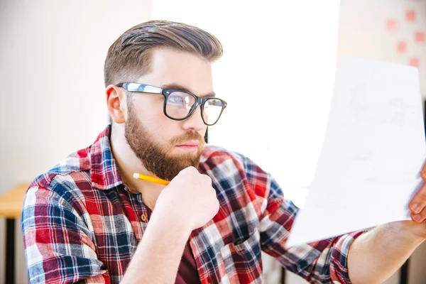 Geconcentreerde man zittend op de werkplek en onderzocht blauwdruk — Stockfoto