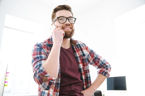 Cheerful young bearded man in glasses talking on mobile phone — Stock Photo, Image