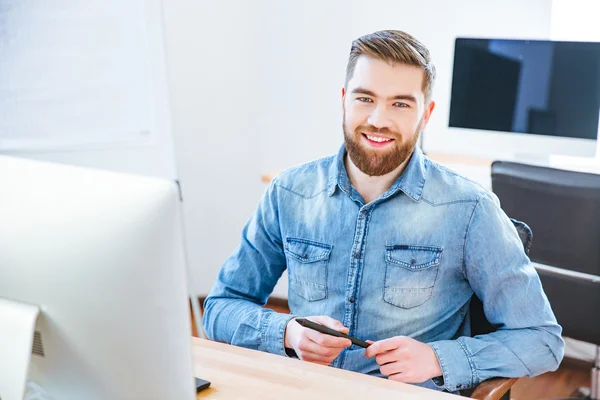 Alegre diseñador guapo sosteniendo lápiz y sentado en la oficina — Foto de Stock