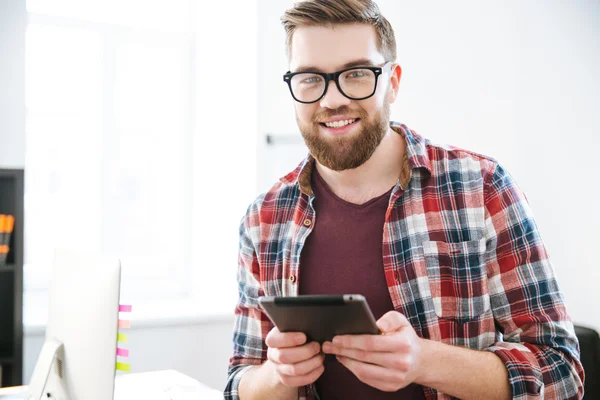 Bonito macho barbudo feliz em óculos usando tablet — Fotografia de Stock