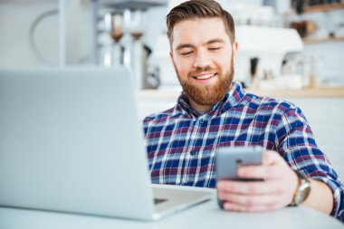 Kafede smartphone ve laptop compute kullanan adam