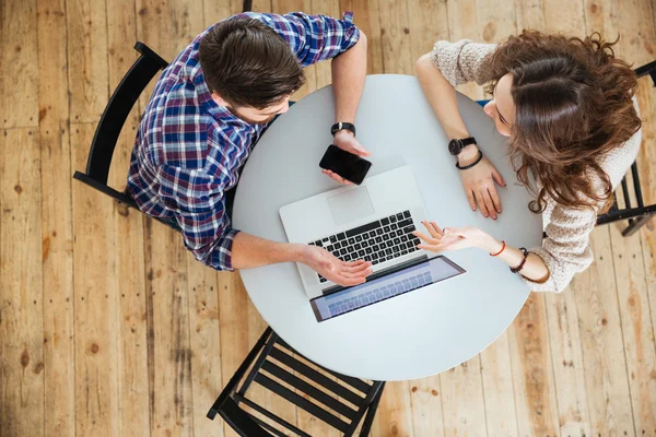 Pareja usando el ordenador portátil y la celebración de la pantalla en blanco del teléfono celular en la cafetería — Foto de Stock