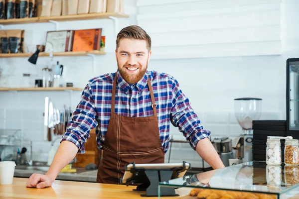 Joyeux beau barista en chemise à carreaux et tablier marron — Photo