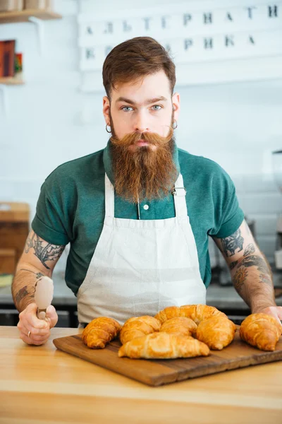 Bonito barista barbudo com croissants no café — Fotografia de Stock