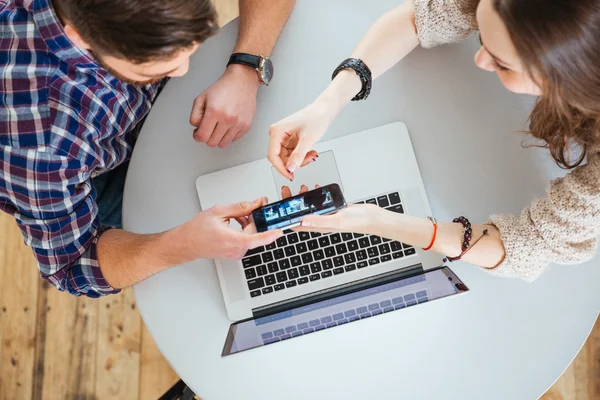 Hombre y mujer mostrando la pantalla del teléfono inteligente sentado en la mesa — Foto de Stock