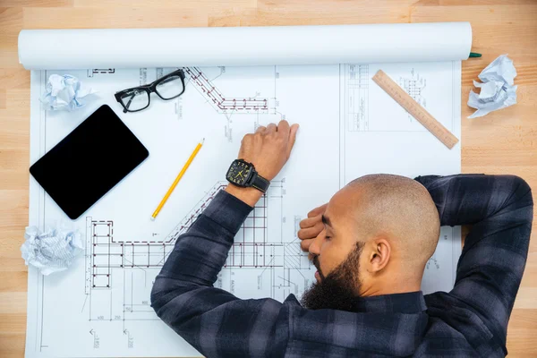 Junger männlicher Designer liegend und schlafend auf Tisch mit Blaupause — Stockfoto