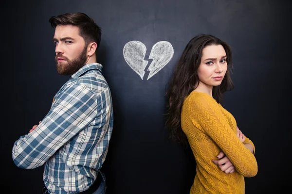 Couple malheureux debout sur fond de tableau noir avec le cœur brisé dessiné — Photo