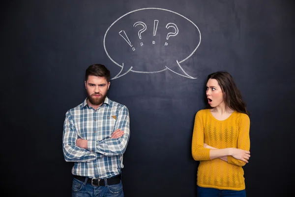 Frowning couple standing after argument over chalkboard background — Stock Photo