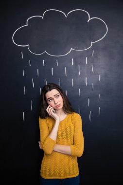 Disappointed woman talking on cellphone under rain drawn at blackboard 
