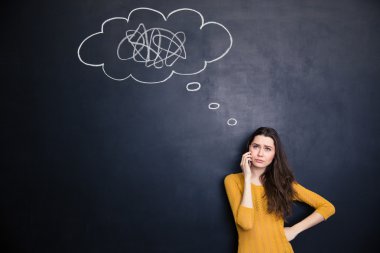 Unhappy woman talking on cellphone standing over background of chalkboard