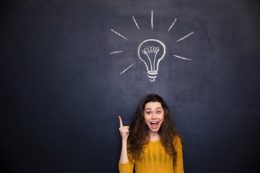 Cheerful woman with opened mouth having idea over blackboard background